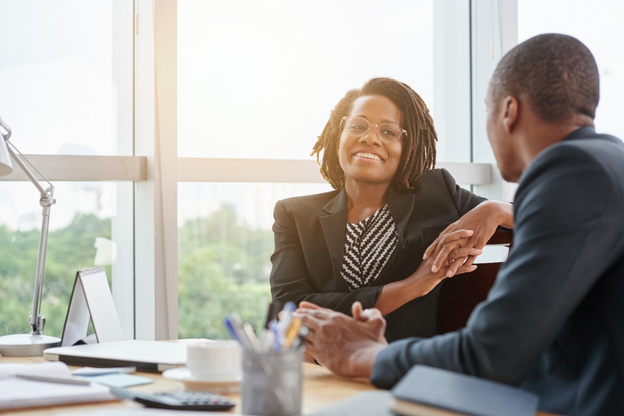 Photo of a man and woman in business suits talking at an office desk