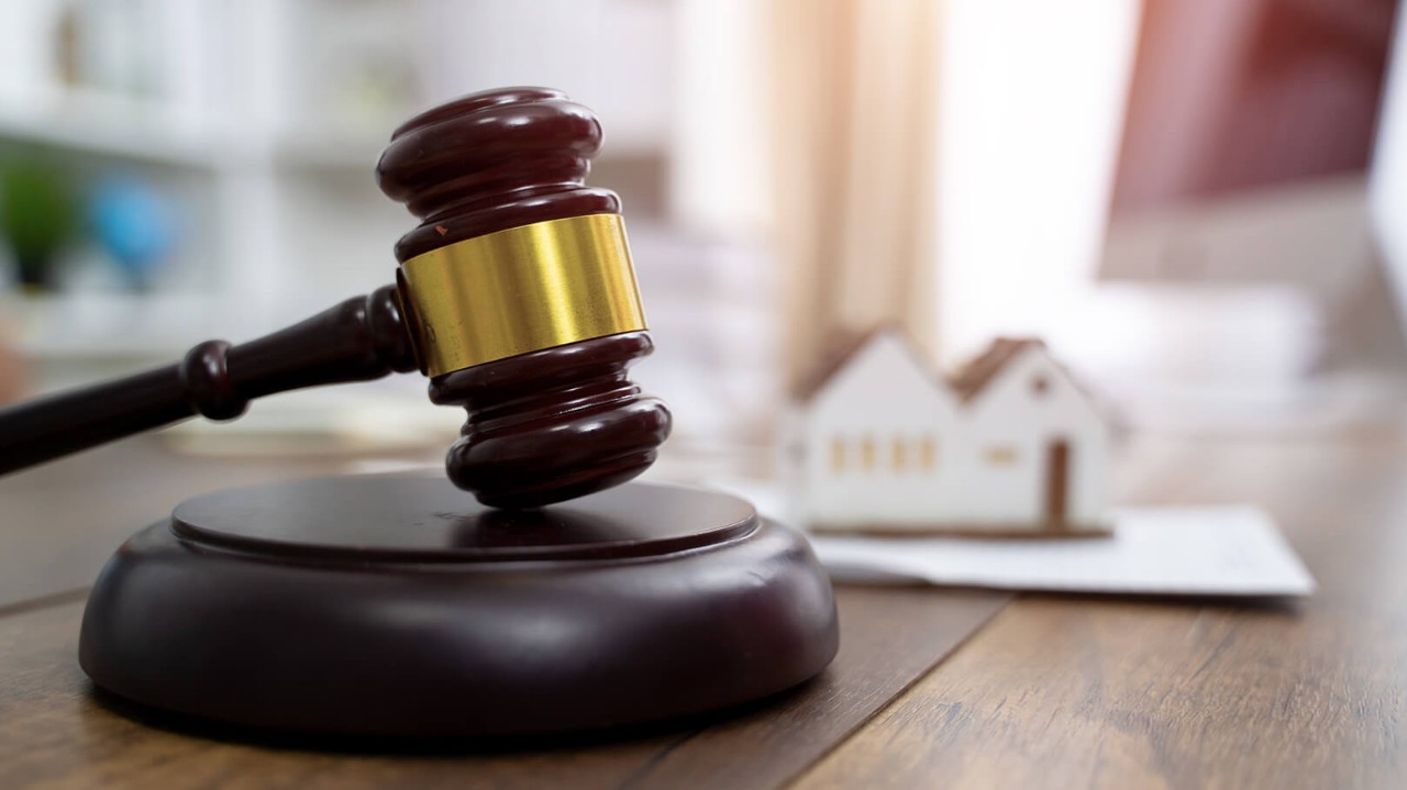 auctioneers gavel in front of a model of a house being used at a housing auction